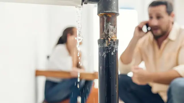 Two people on the phone beside a leaking pipe in a home