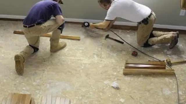 Two workers kneeling on a subfloor while installing new flooring after water damage